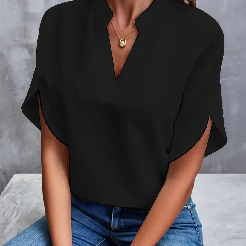 Blouse noire élégante avec col en V, manches courtes, portée par une femme assise en jean. Mode féminine chic, tenue décontractée tendance.