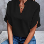 Blouse noire élégante avec col en V, manches courtes, portée par une femme assise en jean. Mode féminine chic, tenue décontractée tendance.
