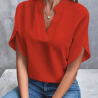 Blouse rouge élégante avec col en V, manches courtes, portée par une femme assise en jean. Mode féminine, tenue chic, style décontracté.