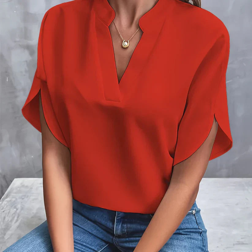 Blouse rouge élégante avec col en V, manches courtes, portée par une femme assise en jean. Mode féminine, tenue chic, style décontracté.