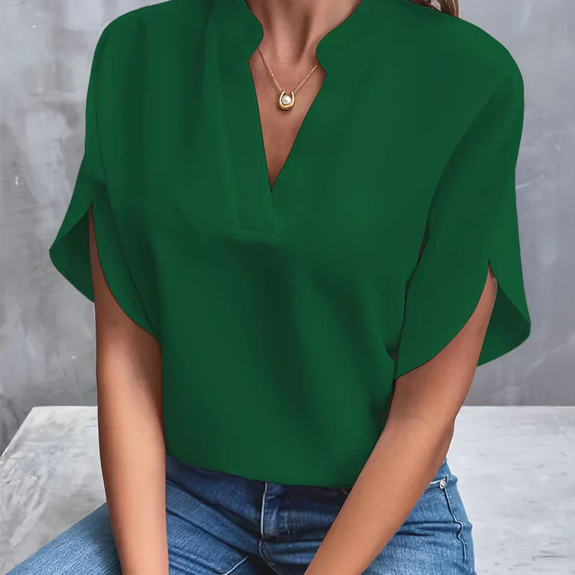 Blouse verte élégante avec col en V, manches courtes, portée par une femme assise en jean. Mode féminine, tenue décontractée chic.