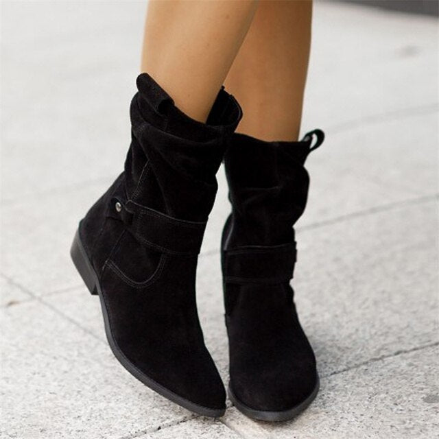 Bottes noires en daim pour femme sur trottoir, style décontracté, talon bas, mode automne-hiver, chaussures élégantes et confortables.