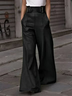 Pantalon large noir femme, taille haute avec ceinture, style urbain chic, rue pavée en arrière-plan, mode élégante et moderne.
