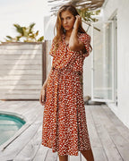 Robe longue à pois blancs sur fond rouge, portée par une femme sur une terrasse en bois près d'une piscine, style estival chic et décontracté.