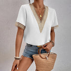 Femme portant un haut blanc à col en V avec dentelle dorée, short en jean, et tenant un sac en osier. Mode estivale chic et décontractée.