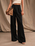 Femme portant un pantalon noir large et un haut blanc, tenant un sac à main beige. Mode élégante, style minimaliste, tenue chic.