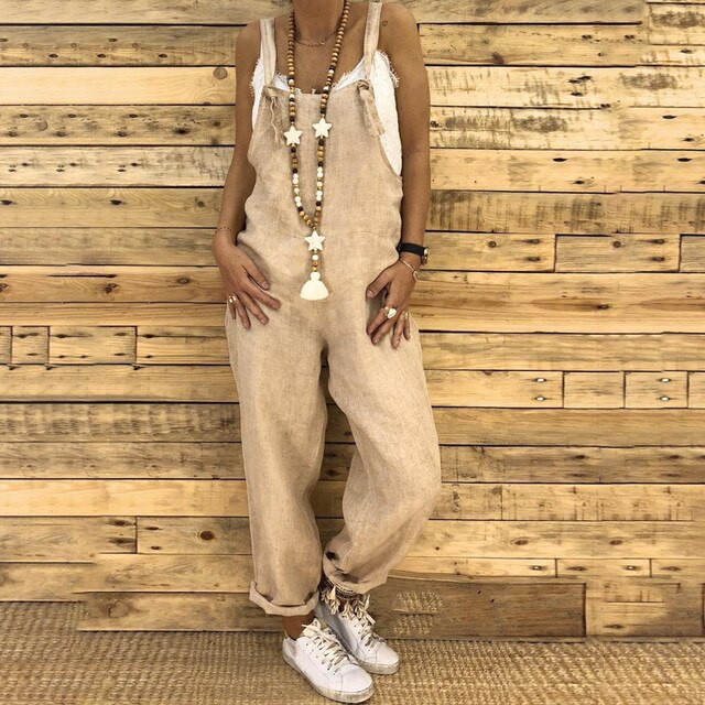 Combinaison en lin beige, femme debout devant un mur en bois, collier long avec pendentifs étoiles, baskets blanches. Mode décontractée chic.
