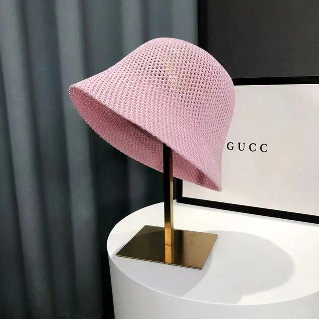 Chapeau cloche rose en tricot sur support doré, devant une boîte Gucci. Accessoire de mode élégant et tendance, idéal pour l'été.