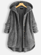 Veste en laine grise à capuche, boutons en bois, manches longues retroussées, texture matelassée, suspendue sur un cintre en bois.