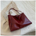 Sac à main en cuir rouge sur un manteau beige, posé sur un lit. Accessoire élégant et tendance, idéal pour un look chic et moderne.