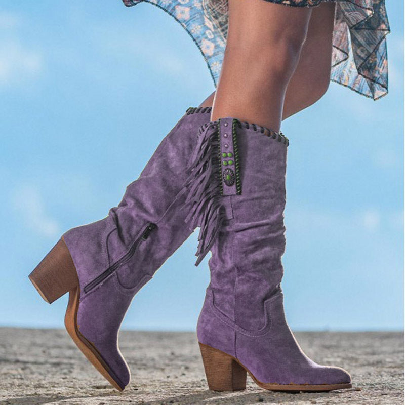 Bottes violettes en daim avec franges et talons blocs, portées par une femme sur fond de ciel bleu. Mode féminine, chaussures tendance.