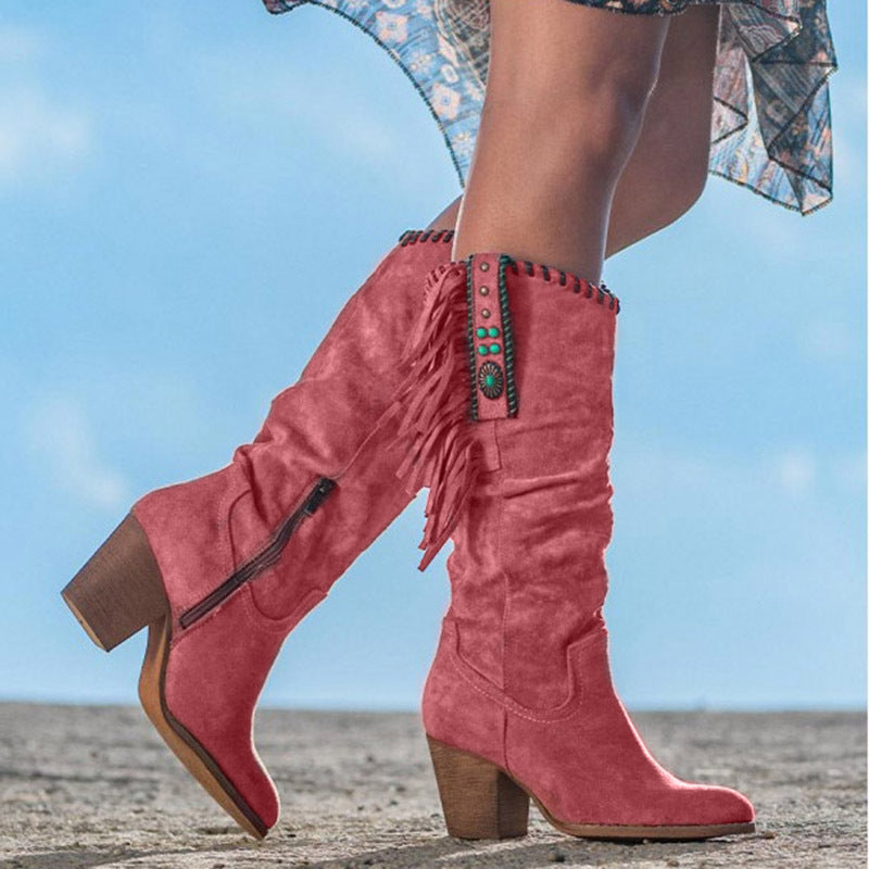 Bottes western roses en daim avec franges et talons blocs, ornées de perles turquoise, portées en extérieur sur fond de ciel bleu.