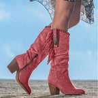Bottes western roses en daim avec franges et talons blocs, ornées de perles turquoise, portées en extérieur sur fond de ciel bleu.
