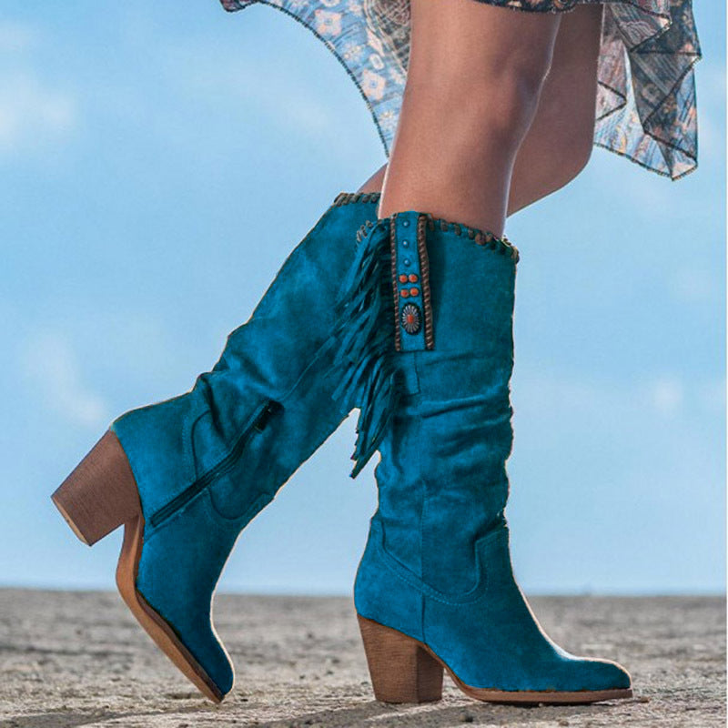 Bottes western bleues en daim avec franges et talons carrés, portées par une femme sur fond de ciel bleu. Mode féminine, style cowboy chic.