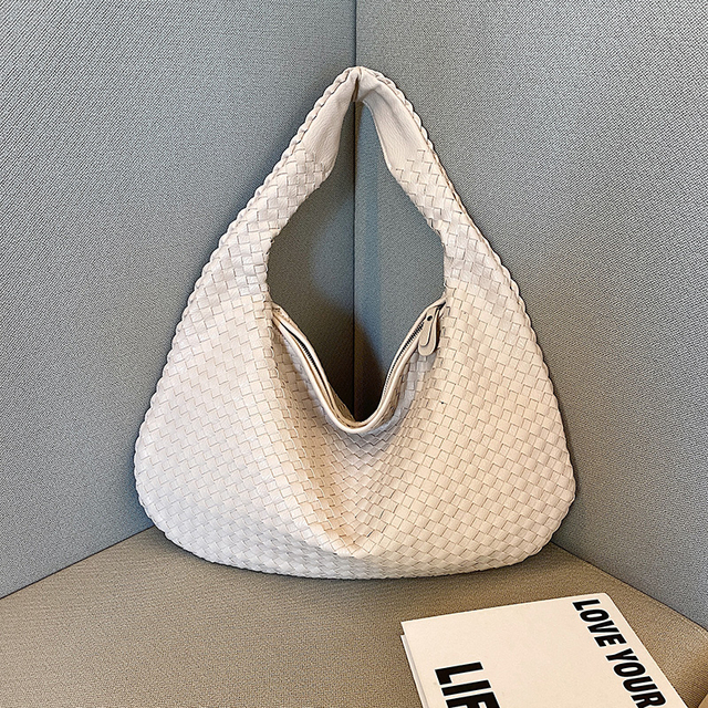 Sac à main blanc tressé en cuir, design moderne, posé sur un canapé gris. Accessoire mode élégant, tendance, idéal pour un look chic et sophistiqué.