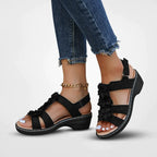 Sandales noires à talons bas avec fleurs, portées avec un jean déchiré. Chaîne de cheville dorée. Mode estivale élégante et confortable.