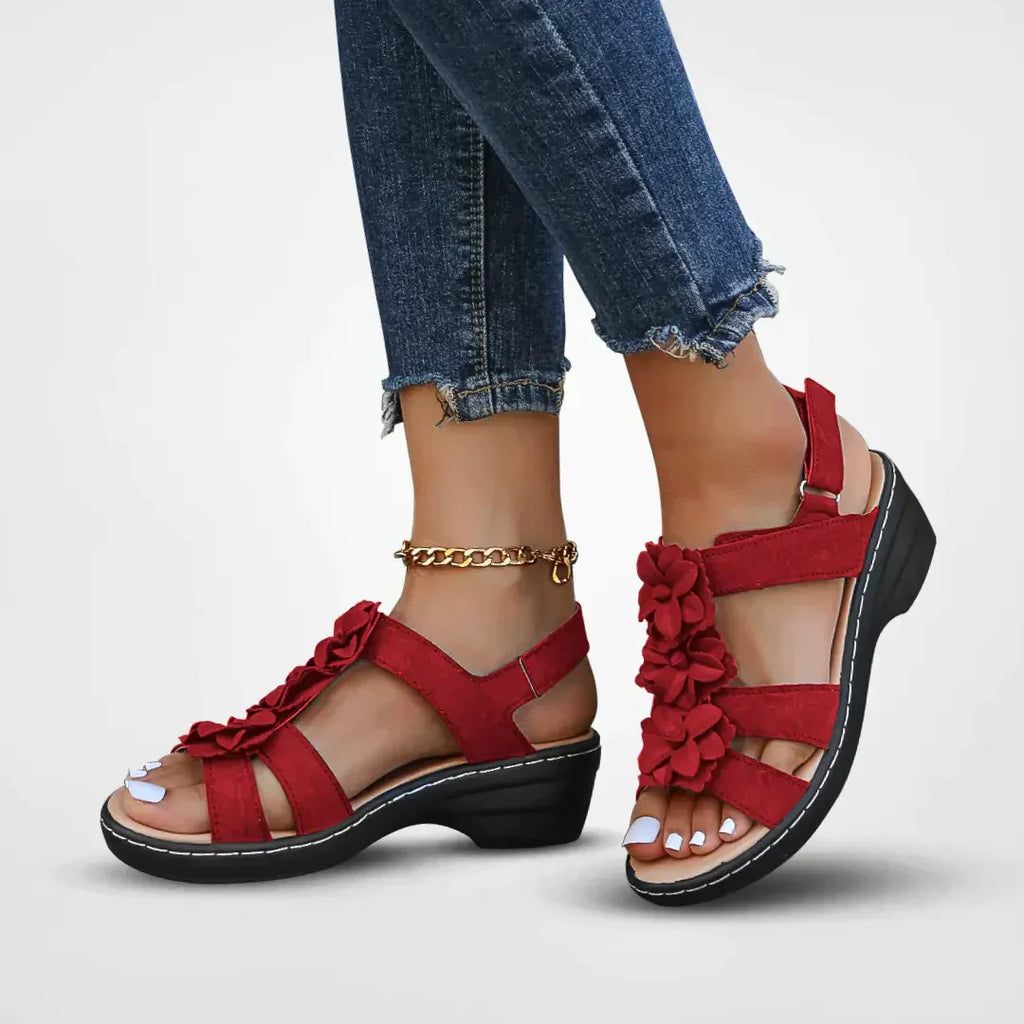 Sandales rouges à fleurs pour femme, talon compensé, portées avec un jean déchiré. Chaussures d'été élégantes et confortables.