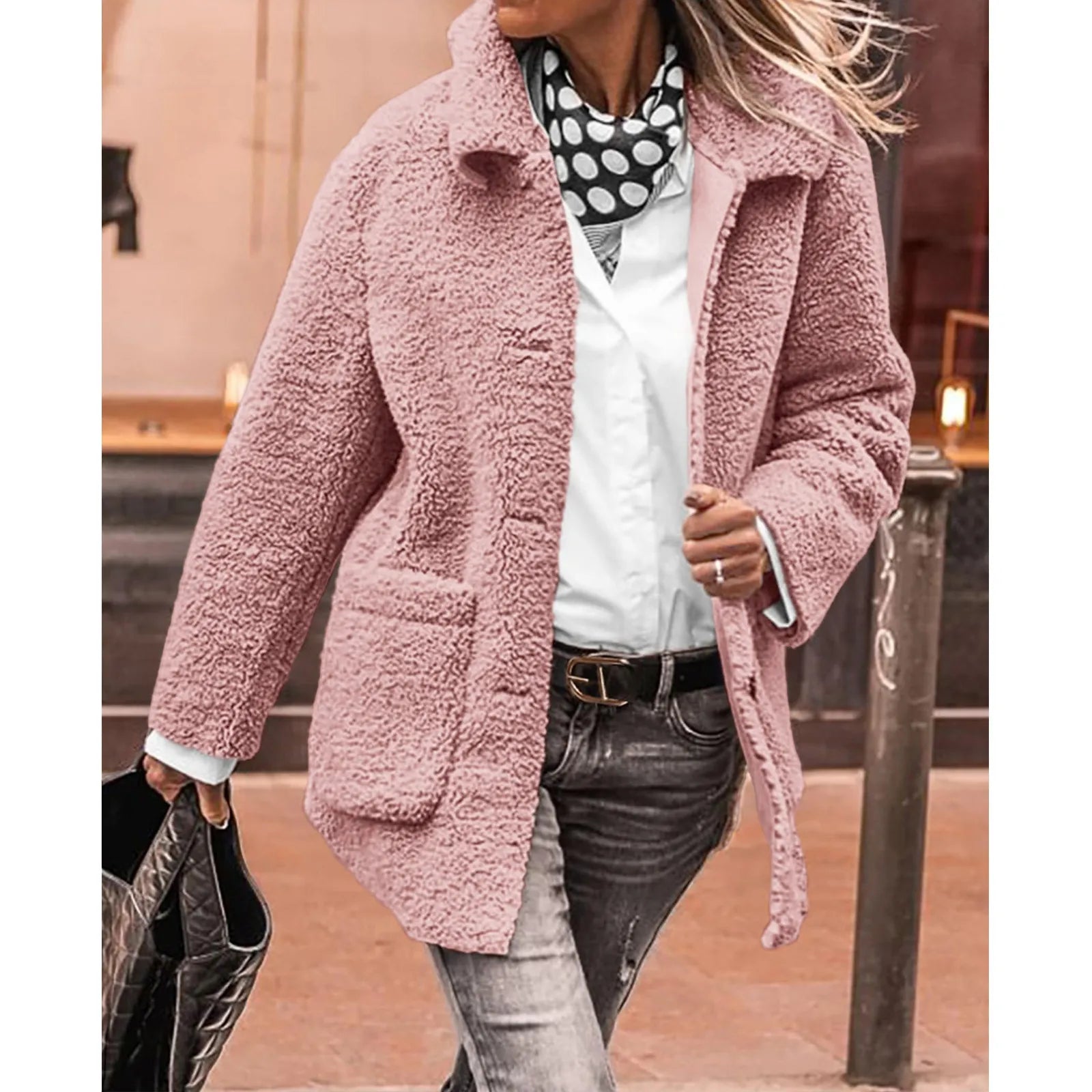 Femme portant un manteau en fausse fourrure rose, chemise blanche, écharpe à pois, jean délavé, sac à main noir. Mode automne-hiver tendance.