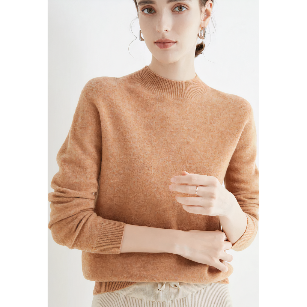 Femme portant un pull en laine beige, manches longues, col rond, posant contre un fond blanc. Mode automne-hiver, style élégant et décontracté.