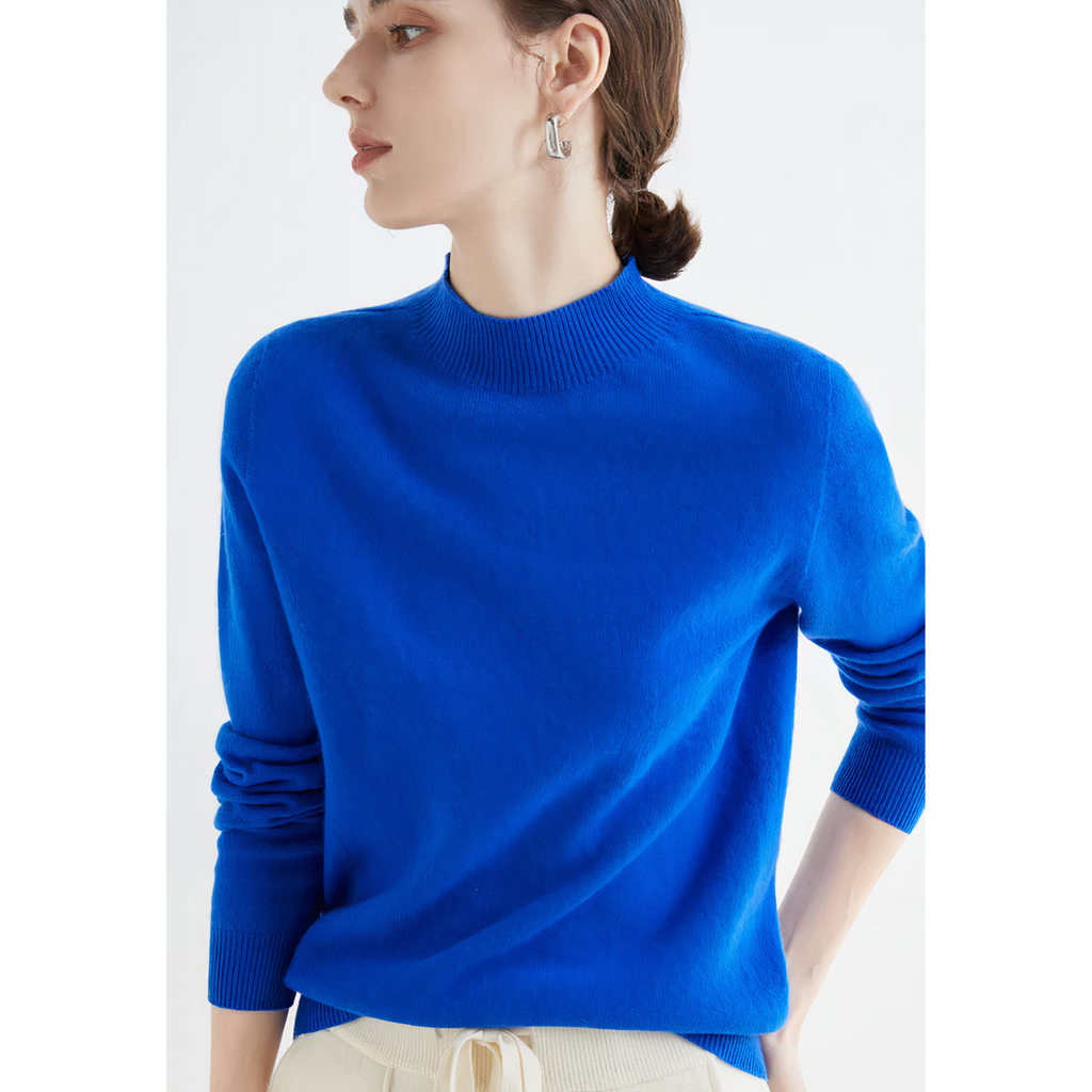 Femme portant un pull bleu vif, manches longues, col rond, avec des boucles d'oreilles argentées, posant de profil. Mode élégante et moderne.