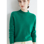 Femme portant un pull vert en cachemire, manches longues, col rond, avec pantalon blanc. Mode élégante, tendance automne-hiver, vêtements confortables.