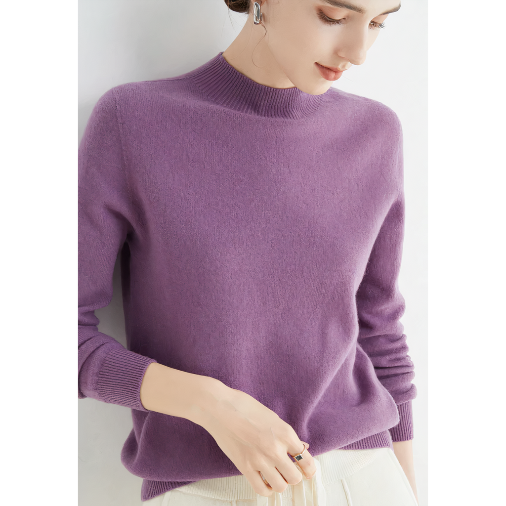 Femme portant un pull violet en cachemire, manches longues, col montant, avec un pantalon blanc. Mode élégante et confortable pour l'hiver.