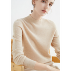 Femme portant un pull beige en laine, assise sur une chaise en bois. Mode automne-hiver, style élégant et minimaliste. Accessoire: boucles d'oreilles.