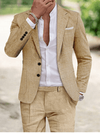 Homme en costume beige élégant, chemise blanche ouverte, montre argentée, bracelet en métal, posant en extérieur. Mode masculine chic et moderne.