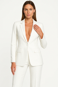 Femme portant un tailleur blanc élégant, veste ajustée et pantalon assorti, sur fond blanc. Mode féminine, tenue professionnelle chic.