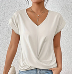 Femme portant un t-shirt blanc à col en V, manches courtes, avec colliers dorés superposés, devant un mur texturé. Mode décontractée élégante.