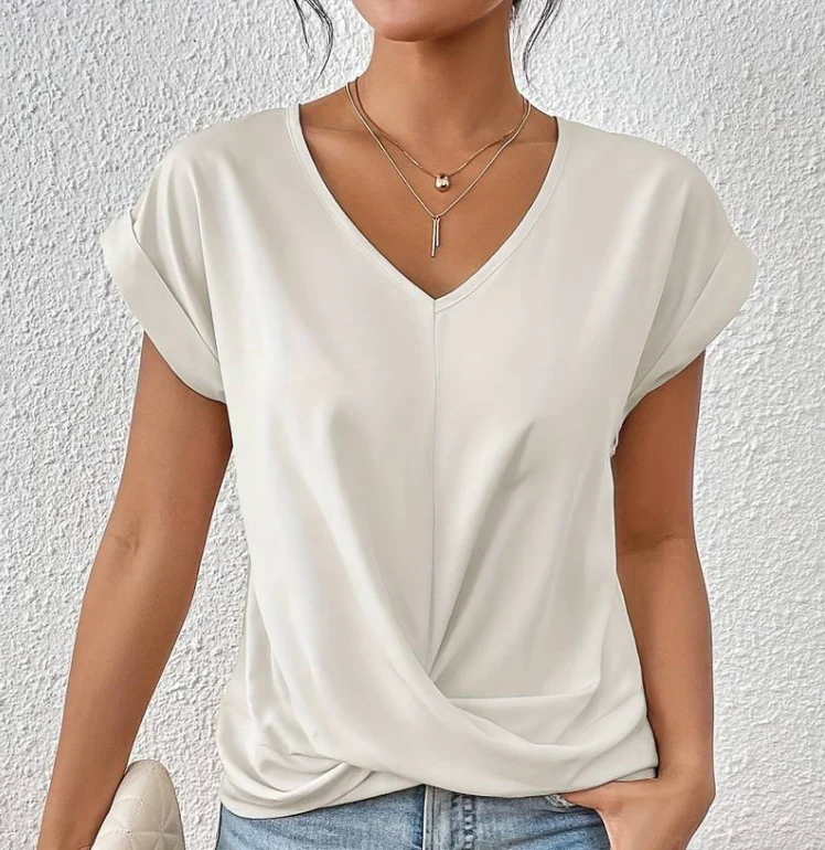 Femme portant un t-shirt blanc à col en V, manches courtes, avec colliers dorés superposés, devant un mur texturé. Mode décontractée élégante.