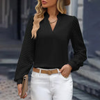 Femme portant un chemisier noir élégant avec manches longues, chapeau beige, ceinture marron, et pantalon blanc. Mode féminine chic et moderne.