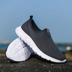 Chaussures de sport noires en maille respirante avec semelles blanches, posées sur un rocher, idéales pour la course et le fitness en plein air.
