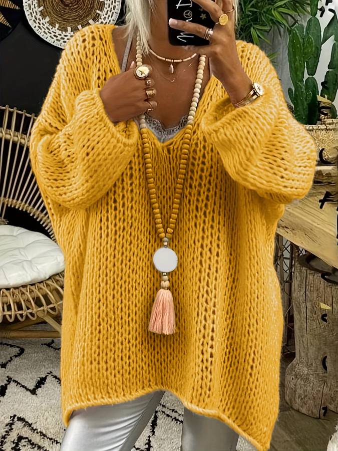 Femme portant un pull oversize jaune en maille, collier long avec pompon, posant devant un miroir. Mode automne, style décontracté, tendance 2023.