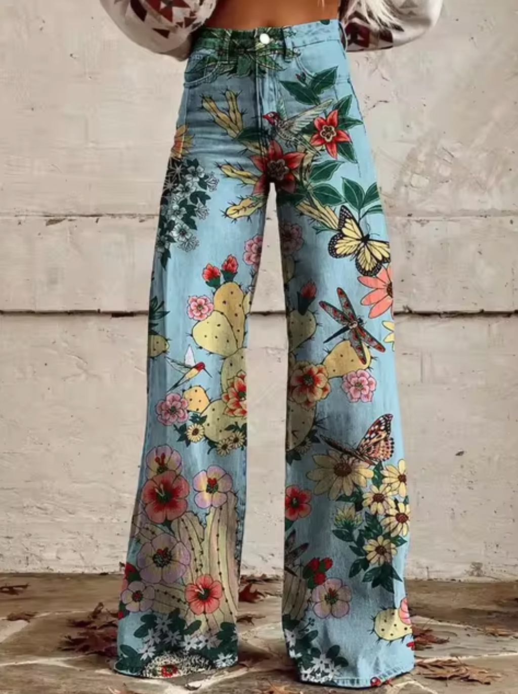 Jean évasé à motifs floraux et papillons colorés sur fond bleu, style bohème chic, idéal pour mode printemps-été, tendance et original.