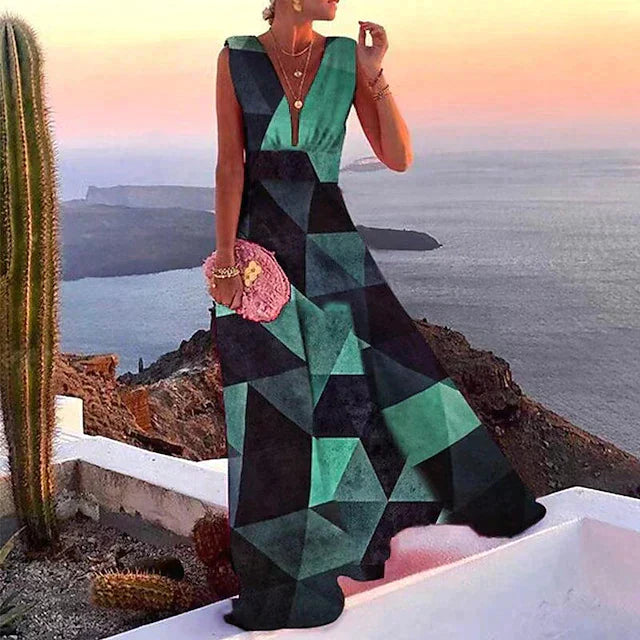 Robe longue géométrique verte et noire, femme debout sur terrasse avec vue sur mer et coucher de soleil, cactus en arrière-plan.