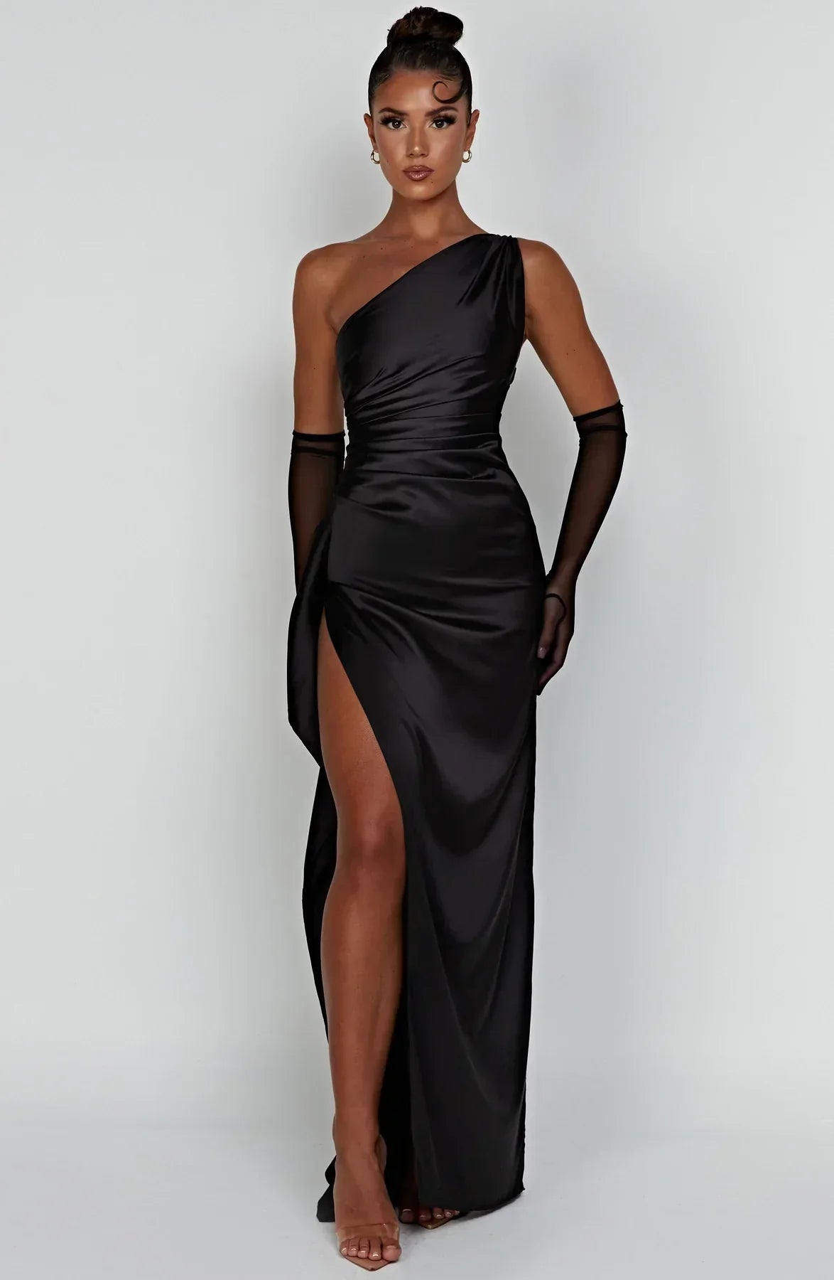 Robe de soirée noire asymétrique avec fente haute, portée par une femme. Élégante et moderne, idéale pour événements formels et soirées glamour.