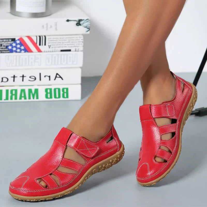 Chaussures rouges en cuir pour femme, design ajouré, semelle antidérapante, confortables et élégantes, posées devant des livres sur une étagère.