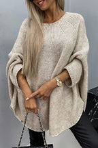 Femme portant un pull oversize beige en tricot, manches longues, avec montre dorée et sac à chaîne noire. Mode automne-hiver tendance.