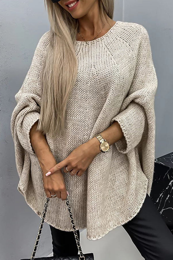 Femme portant un pull oversize beige en tricot, manches longues, avec montre dorée et sac à chaîne noire. Mode automne-hiver tendance.