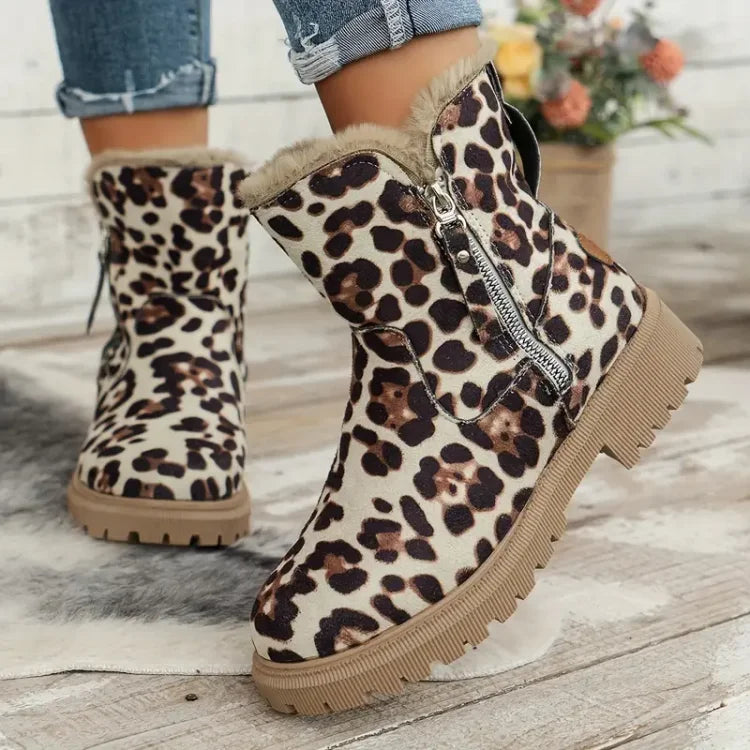 Bottes d'hiver à imprimé léopard avec doublure en fourrure, fermeture éclair latérale, semelle crantée, posées sur un sol en bois, fleurs en arrière-plan.