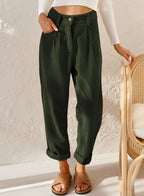 Pantalon vert foncé en tissu côtelé, taille haute, poches avant, ourlets retroussés, porté avec un haut blanc côtelé et des sandales marron.