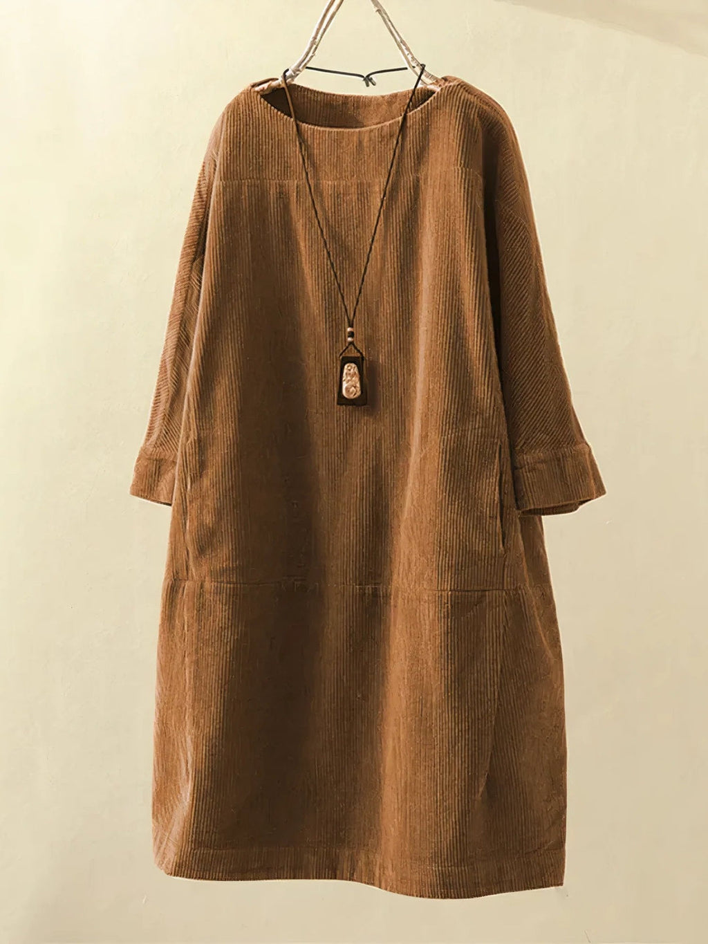 Robe en velours côtelé marron suspendue sur un cintre, avec un collier pendentif en bois. Mode automne, style décontracté, vêtements pour femmes.