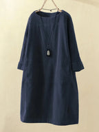 Robe ample en velours côtelé bleu marine, manches longues, col rond, avec pendentif noir suspendu. Mode féminine élégante et décontractée.