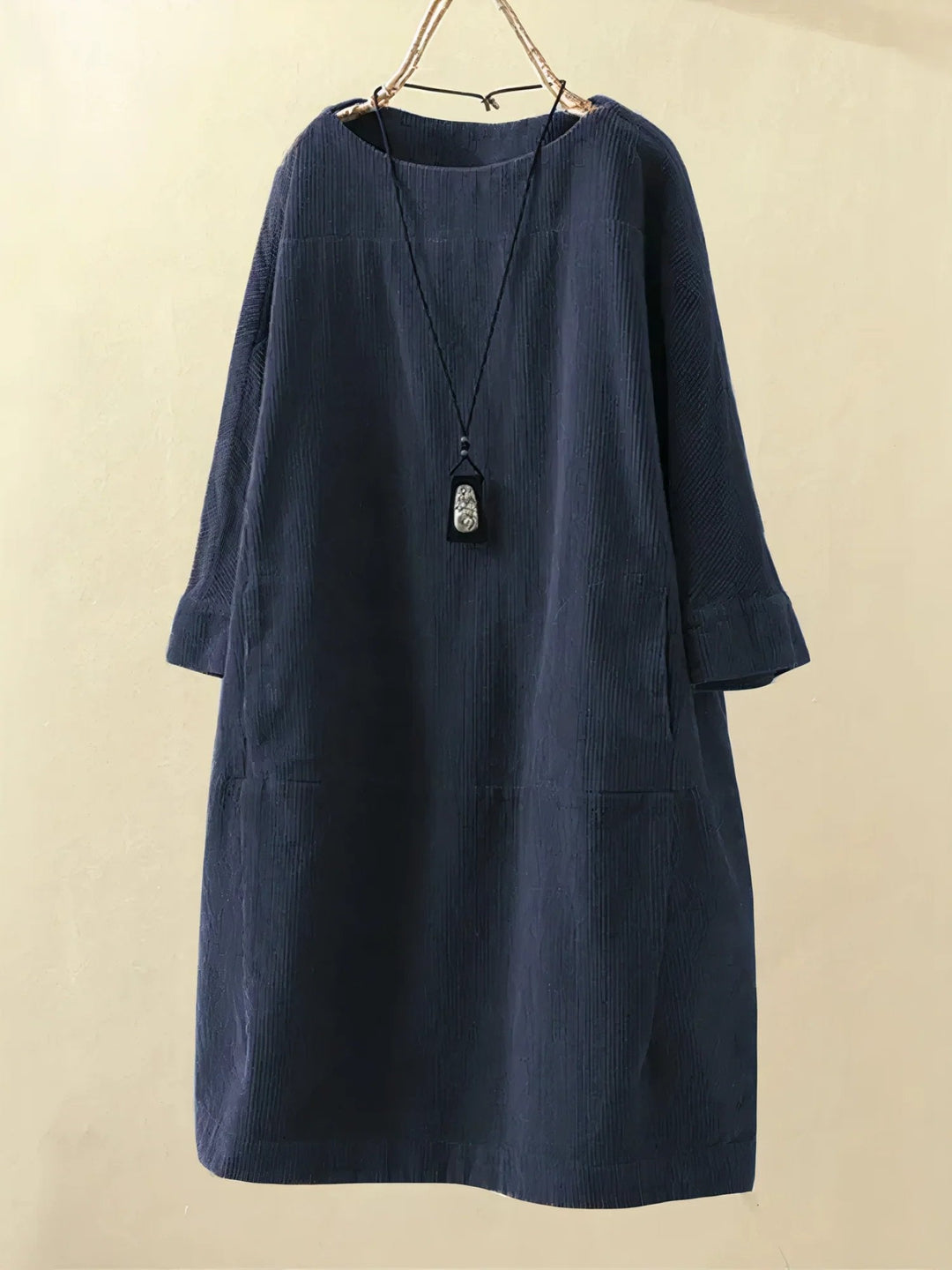 Robe ample en velours côtelé bleu marine, manches longues, col rond, avec pendentif noir suspendu. Mode féminine élégante et décontractée.