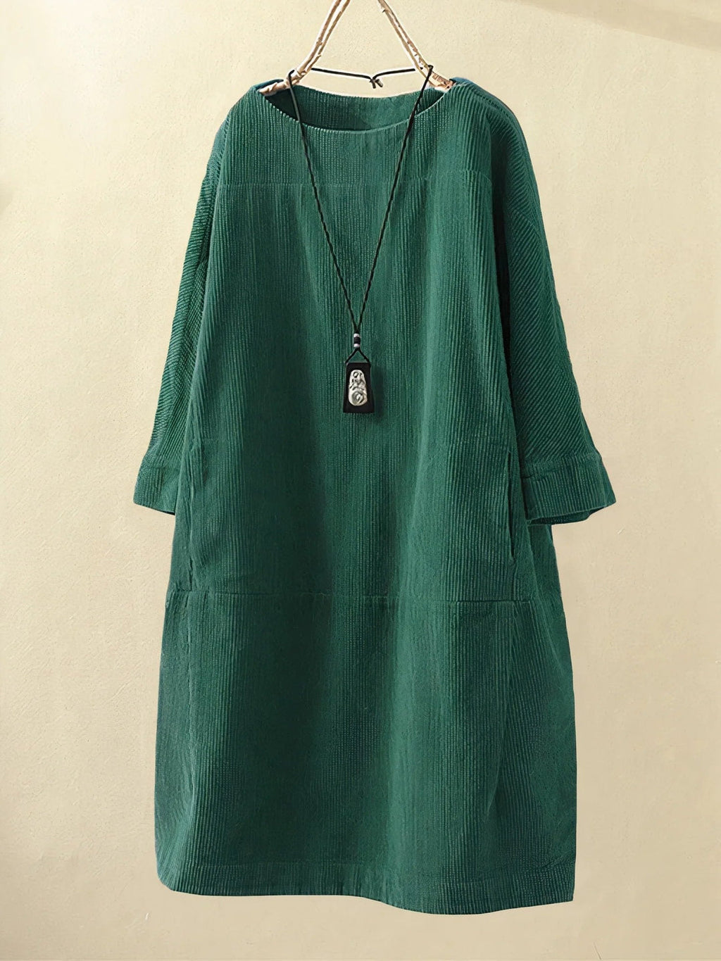 Robe en velours côtelé vert émeraude, manches longues, coupe ample, col rond, avec pendentif noir. Mode féminine élégante et confortable.