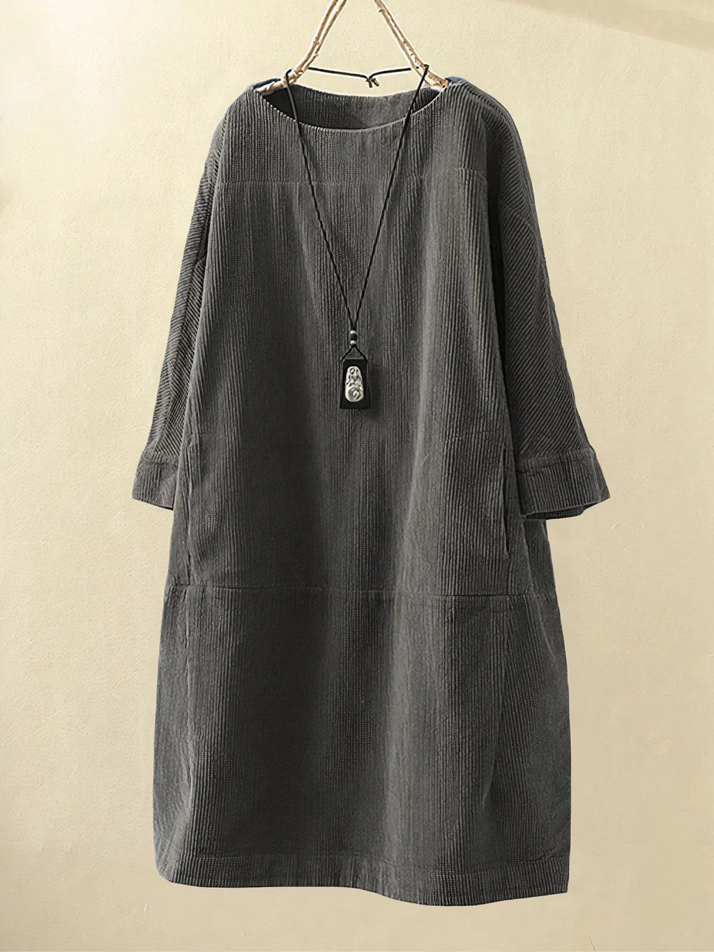 Robe ample en velours côtelé gris avec col rond, manches longues et pendentif noir suspendu. Mode automne-hiver, style décontracté chic.