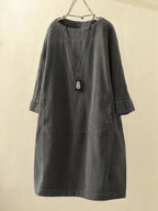 Robe ample en velours côtelé gris avec col rond, manches longues et pendentif noir suspendu. Mode automne-hiver, style décontracté chic.