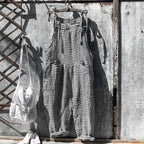 Salopette à carreaux noir et blanc suspendue sur un mur en métal rouillé, sac blanc à côté. Mode vintage, style rétro, vêtements décontractés.