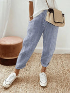 Pantalon rayé bleu et blanc, style décontracté, porté avec un t-shirt blanc, baskets blanches et sac en osier. Mode estivale tendance.